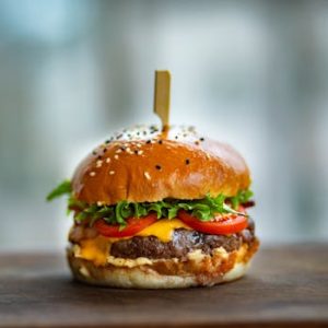 Mouthwatering cheeseburger with fresh tomatoes and lettuce on a wooden surface.